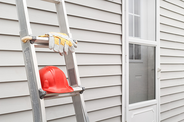 Side of house with light gray siding with a ladder in the foreground