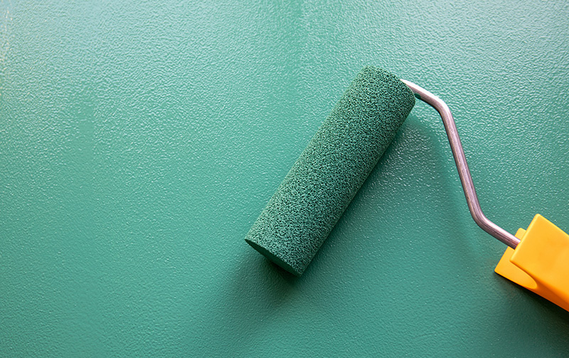 Roller painting jewel toned green paint onto wall